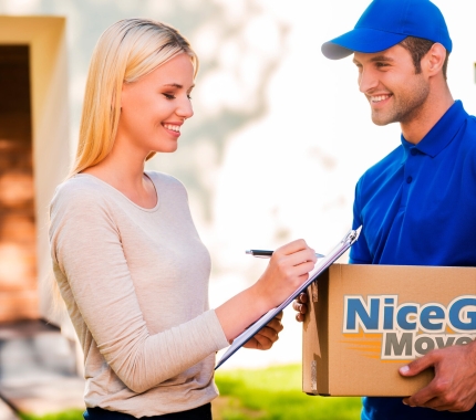 Delivery man holding cardboard box while woman puts signature on clipboard
